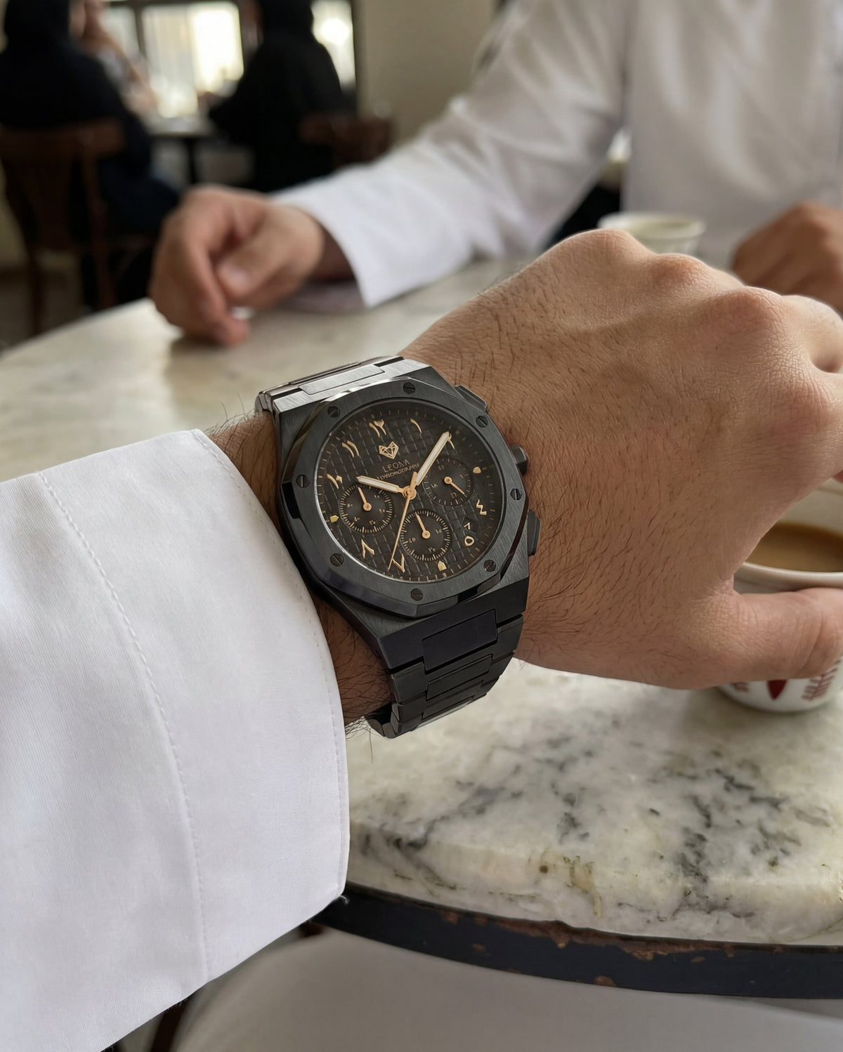 Royal Black Edition Gold on the wrist with a white kandura at a cafe table
