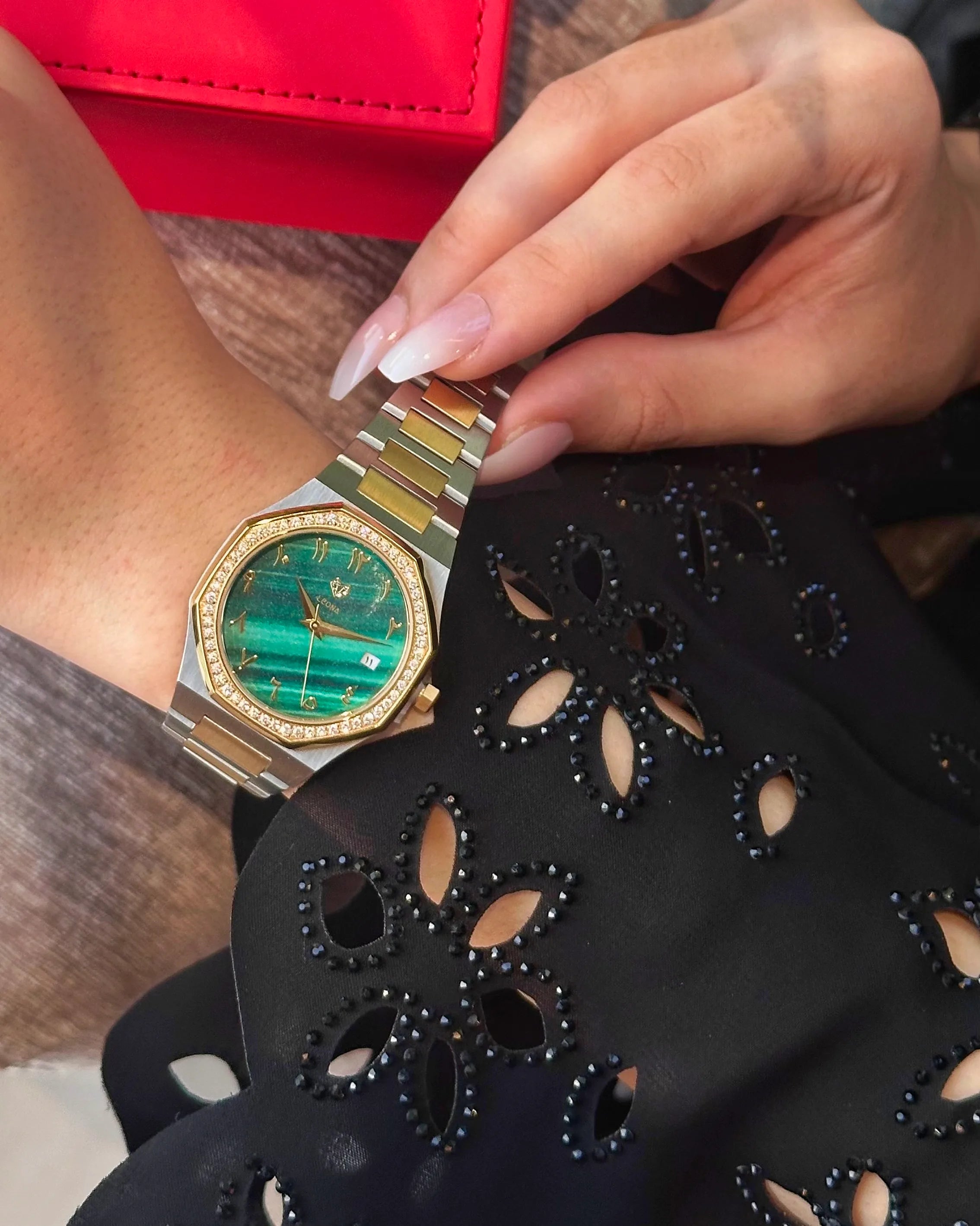 Close-up of a person wearing a silver and green watch on a black floral-patterned surface.