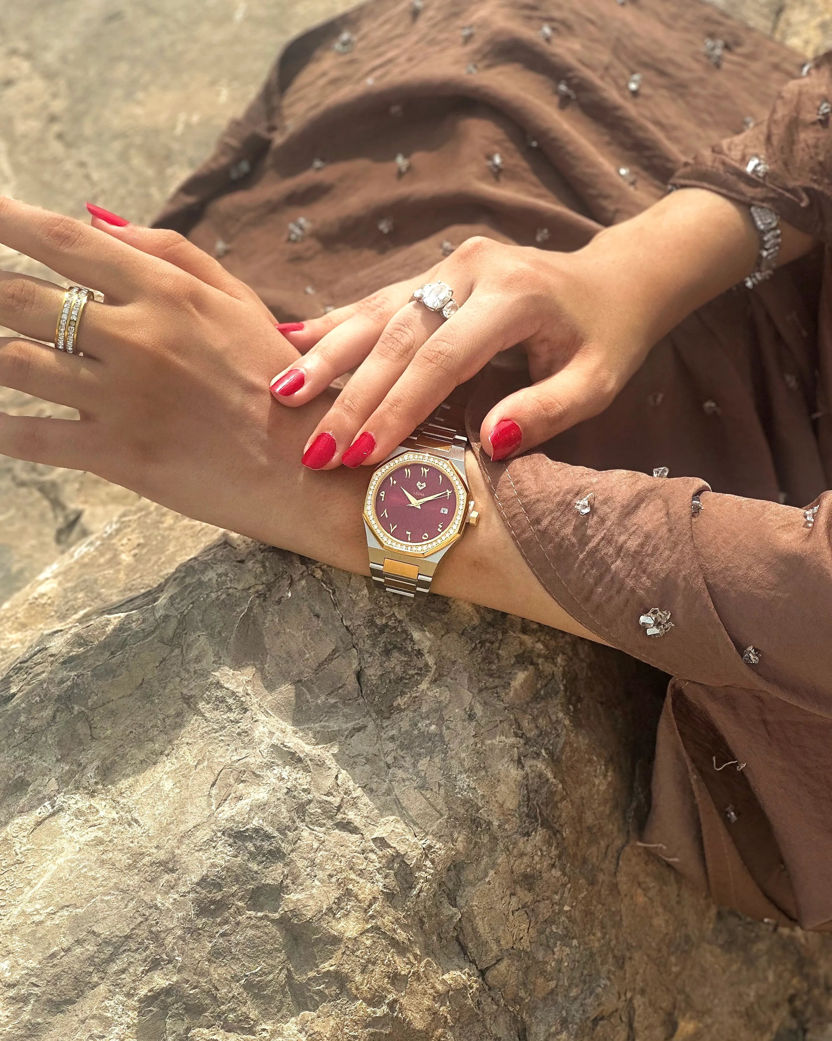 Person wearing a gold watch with a maroon face on a stone surface