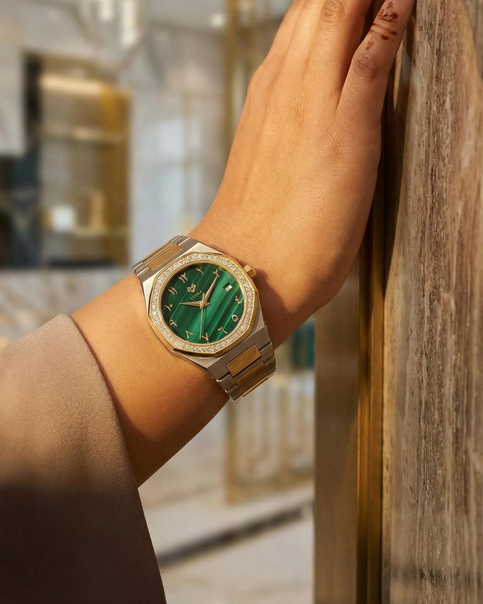 Hand wearing a arabic watch with a green face in an indoor setting