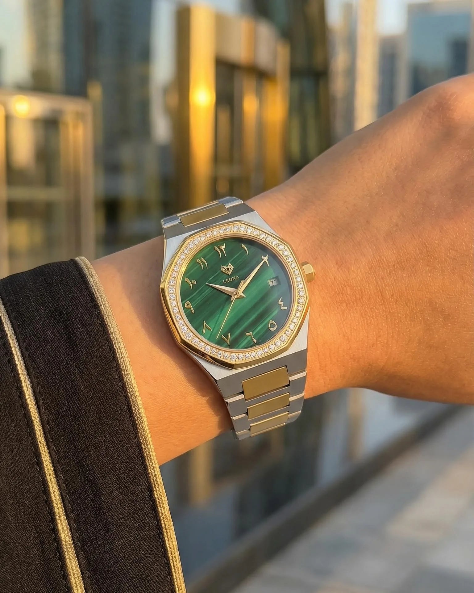 Luxury watch with green face and gold accents on a wrist against a blurred cityscape background