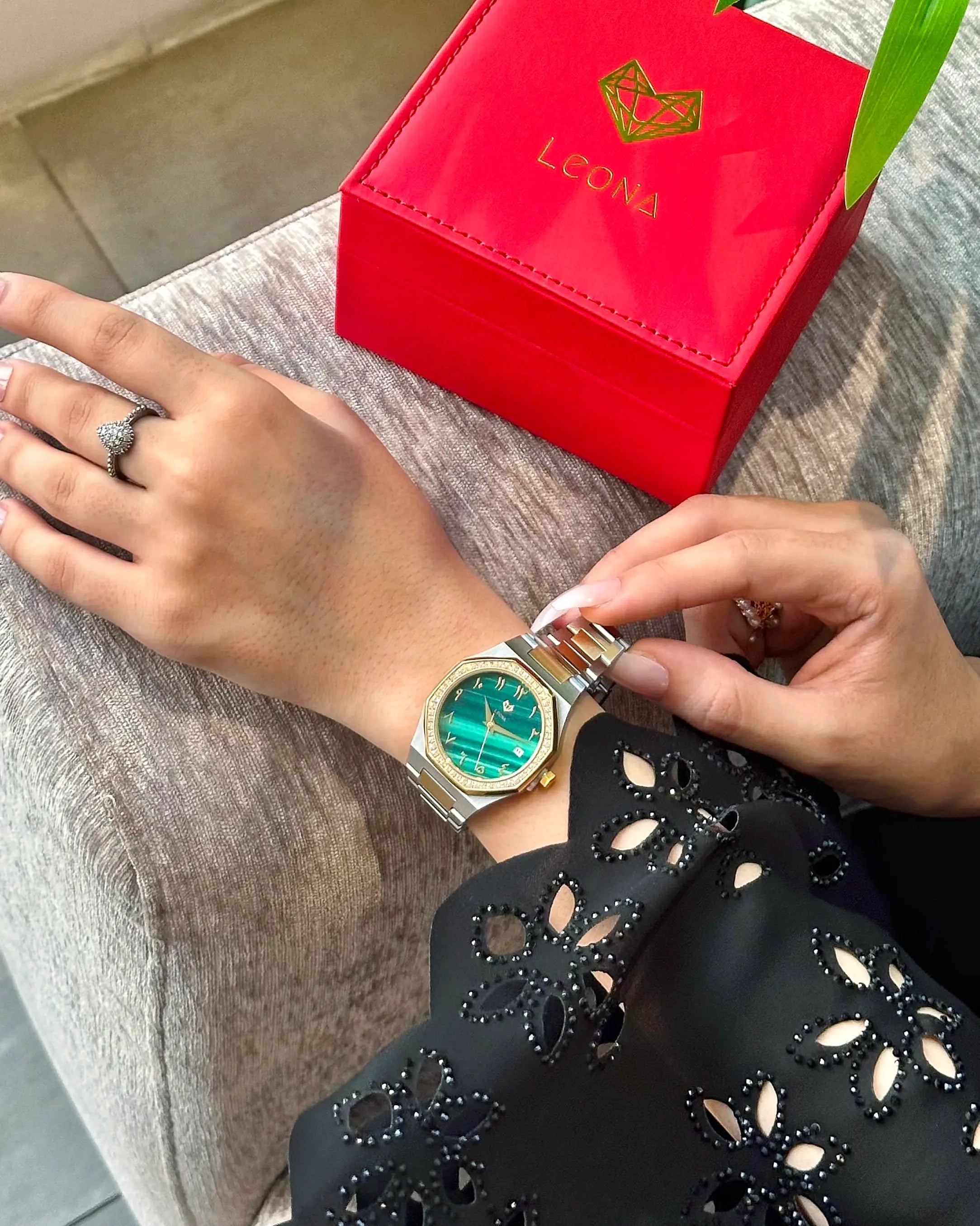 Person wearing a green watch with a red LEONA box on a gray surface