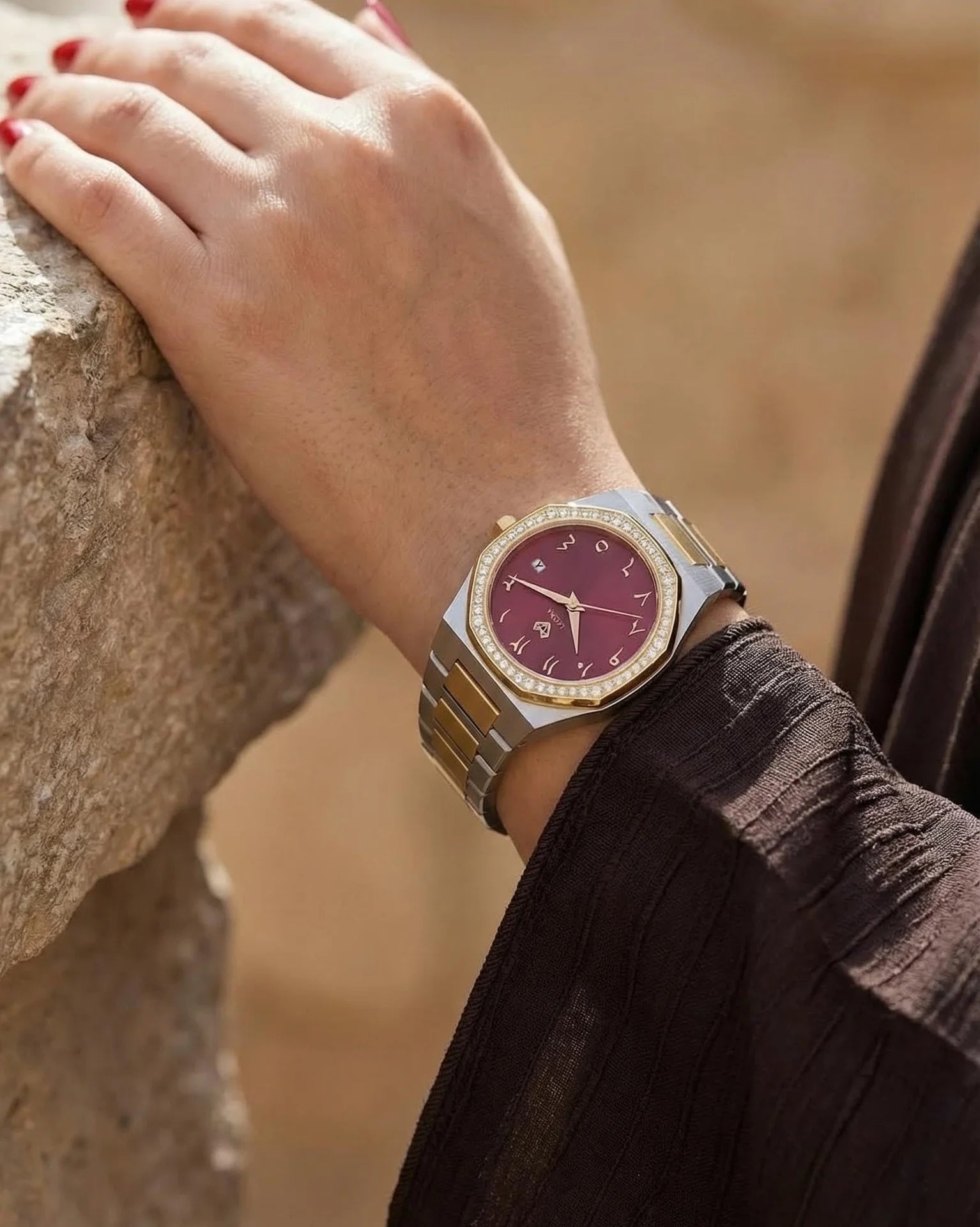 Hand wearing a watch with a red face against a blurred natural background